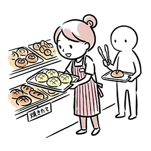 パン屋の売り場で焼きたてパンをトレイから陳列する女性店員とトングを持った客